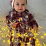 baby, bed, child, christmas, cozy, cute, fairy_lights, festive, foot, hand, holiday, indoors, infant, lighting, lying_down, plaid_pajamas, portrait, santa_hat, smiling, white_bed