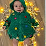 baby, child, christmas_tree_costume, colorful, cute, decoration, fairy_lights, feet, festive, glowing_lights, green_hoodie, happy, holiday, hood, indoors, infant, legs, playful, smiling, wooden_floor