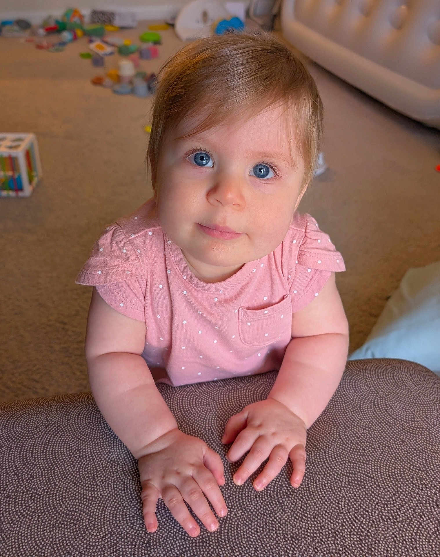 Emma is registered to the contest to win money with this photo: baby, child, infant, pink_shirt, polka_dots, blue_eyes, hands, indoor, carpet, toys, furniture, couch, cute, portrait, young, skin, face, expression, soft_lighting, home