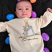 Grayson joined the competition — help win amazing prizes! baby, infant, child, plastic_eggs, colorful, black_blanket, cute, smiling, sweater, bunny_illustration, text_on_clothing, lying_down, indoors, soft_lighting, portrait, happy, young_child, playful, clothing, closeup