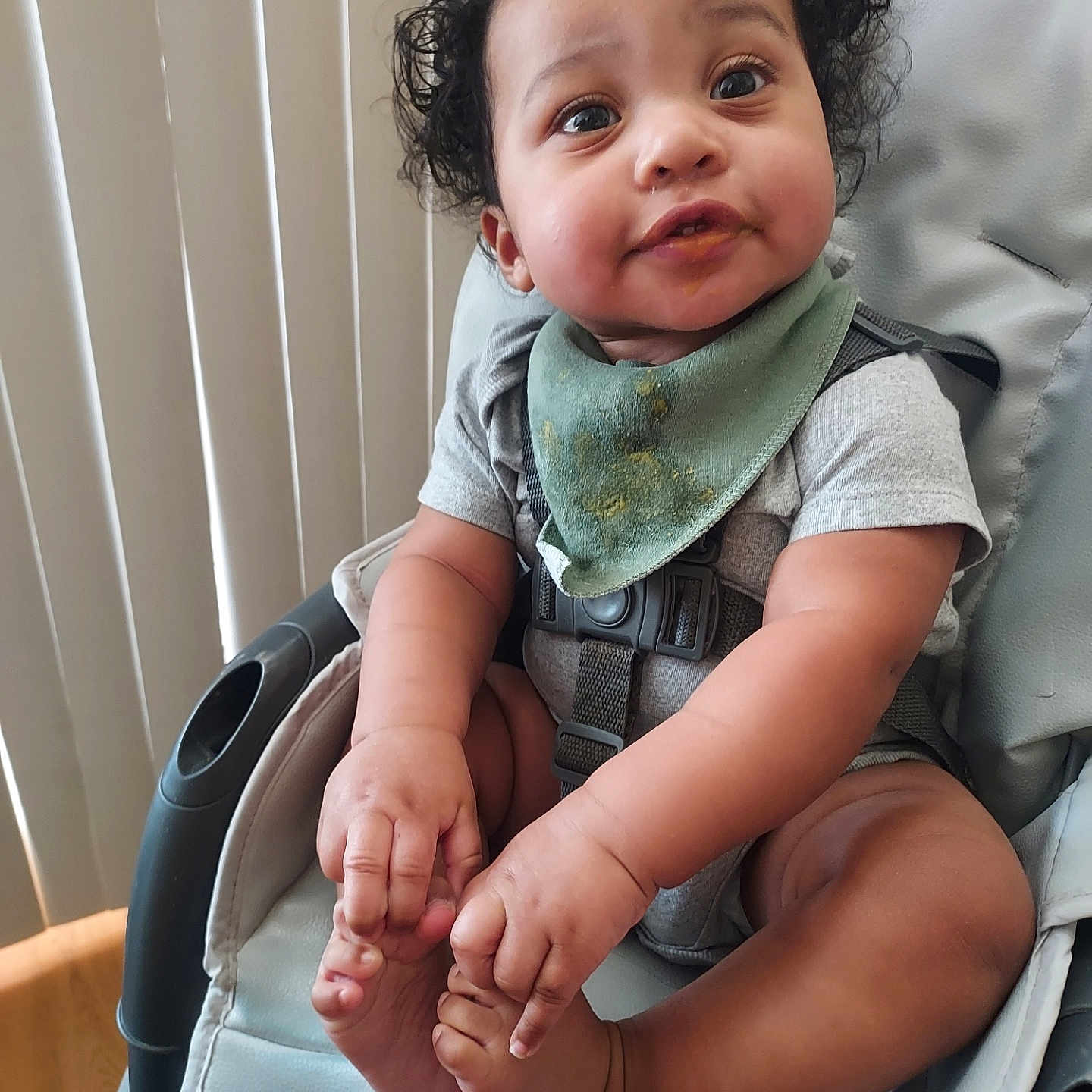 Kai Alon joined the competition — help win amazing prizes! baby, barefoot, bib, child, curious, curly_hair, cute, expression, face, food_stains, foot, gray_clothing, hand, high_chair, indoor, infant, person, playful, seat_belt, skin