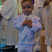 Ewen participe au concours pour gagner de l'argent avec cette photo : child, boy, white_suit, bow_tie, formal_wear, ceremony, indoor, people, adult, priest, white_clothing, shoes, floor, hands, smile, portrait, event, standing, religious, bracelet