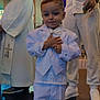child, boy, white_suit, bow_tie, formal_wear, ceremony, indoor, people, adult, priest, white_clothing, shoes, floor, hands, smile, portrait, event, standing, religious, bracelet