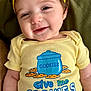 Elodie joined the competition — help win amazing prizes! baby, child, smiling, yellow_headband, yellow_onesie, text_on_clothing, cookie_illustration, face, infant, cute, happy, apparel, headwear, lying_down, cushion, indoor, portrait, closeup, person, funny_text