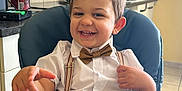 Timothe a rejoint le concours — aidez-le/la à gagner de superbes lots ! child, toddler, smiling, high_chair, bow_tie, suspenders, white_shirt, brown_shorts, kitchen, countertop, paper_towel, utensils, tile_wall, cabinet, happy, indoor, person, cute, playful, hair_spikes