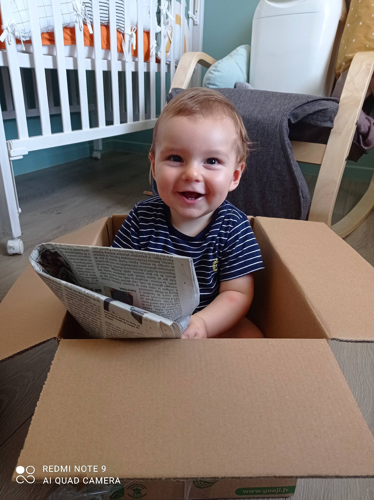 Tilio a rejoint le concours — aidez-le/la à gagner de superbes lots ! box, cardboard, carton, chair, child, comfort, floor, flooring, happy, hardwood, joy, person, room, shipping_box, sitting, smile, standing, t_shirt, table, toddler