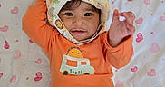 Amira joined the competition — help win amazing prizes! baby, child, infant, portrait, smiling, lying_down, bonnet, orange_outfit, taco_shirt, blanket, heart_pattern, bed, indoor, close_up, face, eyes, hands, casual_clothing, adorable, photography