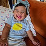 baby, child, smiling, laughing, portrait, indoor, sitting, chair, cushion, bow, headband, short_hair, brown_eyes, clothing, t_shirt, striped_shorts, kitchen, home, furniture, happy
