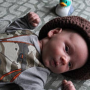 Oakley joined the competition — help win amazing prizes! baby, infant, child, hat, knitted_hat, camouflage_clothing, toy_duck, blanket, texture, fist, curious_expression, lying_down, cute, indoor, soft_lighting, face, head, person, small_hands, playful