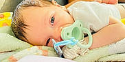 Fabian is registered to the contest to win money with this photo: baby, blanket, child, close_up, comfort, cute, face, hair, indoor, infant, light, lying_down, newborn, pacifier, peaceful, resting, skin, small_hand, soft_texture, white_clothing