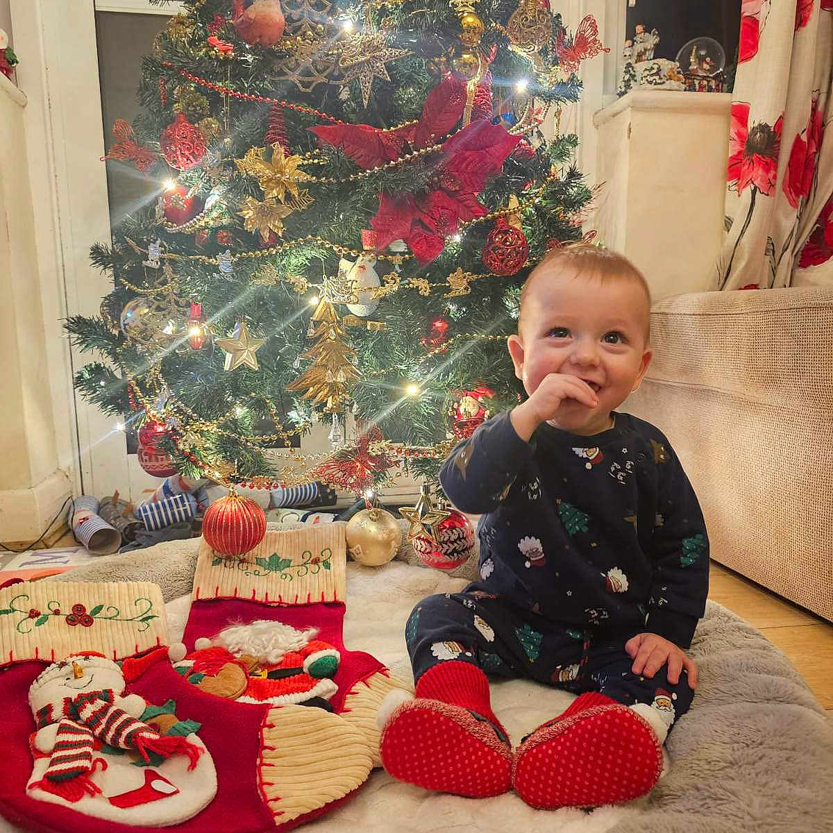 Kaloyan is registered to the contest to win money with this photo: baby, celebration, child, christmas_stockings, christmas_tree, cozy_rug, cute, festive, festive_pajamas, happy, holiday_decorations, holiday_spirit, home, indoor, ornaments, red_and_gold, sitting, smiling_child, twinkling_lights, winter
