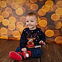 baby, child, sitting, smiling, reindeer_sweater, holiday, christmas, indoors, wooden_floor, bokeh, lights, festive, cute, portrait, red_shoes, blue_pants, long_sleeve, happy, young, background