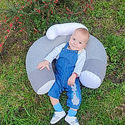 Kaloyan is registered to the contest to win money with this photo: baby, child, outdoor, grass, bush, red_berries, blue_overalls, sneakers, cushion, pillow, happy, smile, person, nature, greenery, casual_clothing, infant, playful, relaxed, daylight