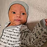 Francesco is registered to the contest to win money with this photo: baby, infant, child, onesie, hat, face, eyes, clothing, text, blanket, lying_down, cute, soft, newborn, portrait, indoors, skin, expression, headwear, closeup