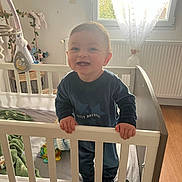 Aaron a rejoint le concours — aidez-le/la à gagner de superbes lots ! toddler, crib, baby, smiling, indoor, nursery, window, curtains, toy, blanket, child, furniture, wooden_floor, wall_decor, radiator, clothing, happy, standing, person, daylight