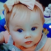 Dana is registered to the contest to win money with this photo: baby, child, face, headband, bow, blue_eyes, clothing, overall, toy, snowman_toy, pink, peach, curious, portrait, closeup, indoor, cute, infant, person, young_child