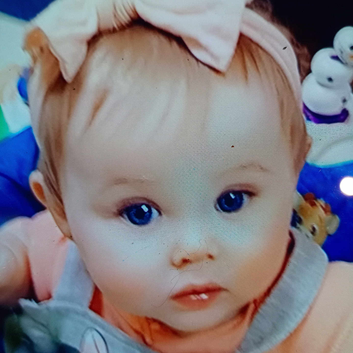 Dana is registered to the contest to win money with this photo: baby, child, face, headband, bow, blue_eyes, clothing, overall, toy, snowman_toy, pink, peach, curious, portrait, closeup, indoor, cute, infant, person, young_child