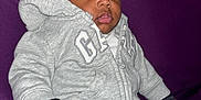 Mason joined the competition — help win amazing prizes! baby, child, hoodie, mittens, gray_clothing, sitting, purple_background, curly_hair, indoor, portrait, casual, cute, young_child, warm_clothing, face, expression, cozy, infant, person, comfort
