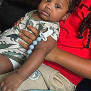 Mason joined the competition — help win amazing prizes! baby, child, infant, dinosaur_onesie, pacifier_clip, blanket, couch, holding, curly_hair, red_shirt, beige_pants, indoors, close_up, comfortable, cute, relaxed, skin, hand, face, portrait