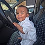 baby, child, car, steering_wheel, car_interior, seat_cover, smiling, white_clothing, cute, happy, portrait, infant, vehicle, dashboard, window, daylight, seat, young_child, sitting, hand