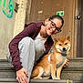 girl, dog, shiba_inu, steps, outdoor, glasses, casual_clothing, harness, smiling, brown_dog, young_person, urban, graffiti, door, stone, pet, friendship, leash, happy, daylight