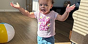 Alaya joined the competition — help win amazing prizes! toddler, child, barefoot, curly_hair, pink_shirt, blue_shorts, indoor, wooden_floor, sunlight, beach_ball, smiling, arms_outstretched, home, living_room, mirror, television, rug, basket, furniture, playful