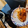 Artemis is registered to the contest to win money with this photo: black_cat, cat, food, plate, fork, cheese, chair, floor, kitchen, curious, pet, animal, table, tile_floor, paper_plate, human_hand, indoor, meal, looking, hungry