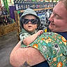 Donovan joined the competition — help win amazing prizes! baby, sunglasses, hat, adult, tattoo, animal_print, store, shelf, shopping, person, holding, smile, child, indoor, clothing, green, blue, cute, accessory, happy