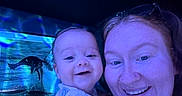 Donovan is registered to the contest to win money with this photo: baby, woman, smile, selfie, blue_light, aquarium, dolphin, face, portrait, child, happy, indoor, glasses, person, short_sleeve, nose_ring, holding, closeup, water, exhibit