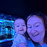 baby, woman, smile, selfie, blue_light, aquarium, dolphin, face, portrait, child, happy, indoor, glasses, person, short_sleeve, nose_ring, holding, closeup, water, exhibit