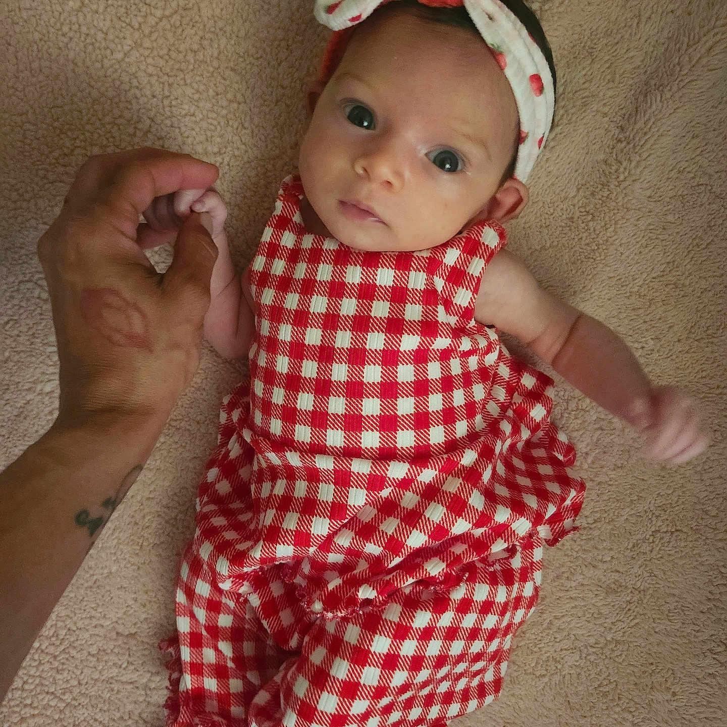 Mireya joined the competition — help win amazing prizes! baby, infant, child, hand, finger, red_checkered_clothing, headband, blanket, skin, person, cute, looking, lying_down, small, newborn, soft_texture, indoor, portrait, holding, adult_hand