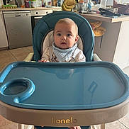 Diégo a rejoint le concours — aidez-le/la à gagner de superbes lots ! baby, high_chair, blue, kitchen, infant, face, child, feeding_chair, window, countertop, bottle, floor, foot, bib, table, domestic, appliance, cup, food_preparation, person