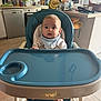 baby, high_chair, blue, kitchen, infant, face, child, feeding_chair, window, countertop, bottle, floor, foot, bib, table, domestic, appliance, cup, food_preparation, person