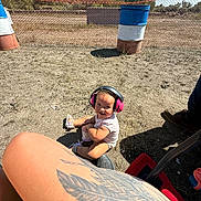 Payton joined the competition — help win amazing prizes! barrel, child, clouds, dirt, fence, grass, happy, headphones, leg, outdoor, person, shadow, shoe, sitting, sky, smiling, sunny, tattoo, toddler, trees