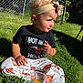 Payton is registered to the contest to win money with this photo: toddler, child, outdoor, grass, sunlight, headband, flower, black_shirt, pants, cow_print, container, snack, cheese_sticks, sitting, greenery, fence, daylight, cute, expression, portrait
