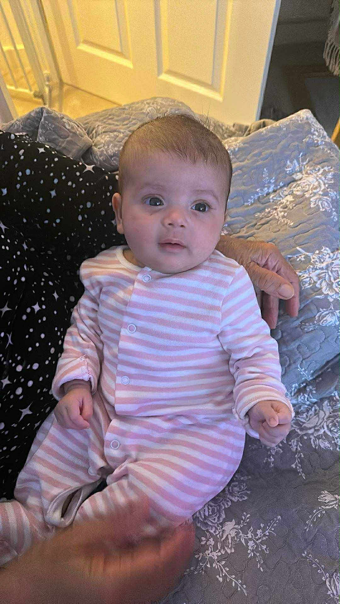 Metiem joined the competition — help win amazing prizes! baby, infant, pink_stripes, quilt, hand, adult_hand, person, indoor, clothing, bedroom, fabric, pattern, sleepwear, cute, newborn, face, sitting, portrait, soft_lighting, young_child