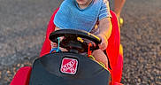 Jaxsyn is registered to the contest to win money with this photo: baby, child, toddler, smiling, happy, outdoor, portrait, vehicle, toy_car, steering_wheel, red_car, blue_shirt, bib, driveway, playtime, summer, family, parked_car, sunlight, face