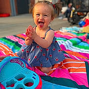 Leyra is registered to the contest to win money with this photo: toddler, child, smiling, clapping, pigtails, dress, outdoor, blanket, colorful, toy, happy, playful, sunlight, portrait, young_child, summer, fun, sitting, daytime, cute