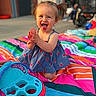 toddler, child, smiling, clapping, pigtails, dress, outdoor, blanket, colorful, toy, happy, playful, sunlight, portrait, young_child, summer, fun, sitting, daytime, cute