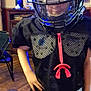 child, football_helmet, sports_gear, indoor, black_clothing, hand_on_hip, wooden_floor, television, furniture, hat, faceguard, silhouette_art, room, person, confident, standing, mesh_jersey, helmet_visor, casual, young