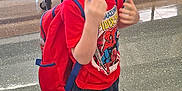 William is registered to the contest to win money with this photo: child, boy, glasses, red_tshirt, spiderman, backpack, school, cafeteria, bench, floor, jeans, sneakers, smiling, person, indoor, kids, people, casual_clothing, young, standing