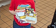 William joined the competition — help win amazing prizes! banana, boy, breakfast, cafeteria, cereal_box, child, floor_tiles, food, glasses, indoor, jeans, person, plastic_baskets, red_carpet, red_shirt, shelves, smiling, sneakers, spiderman, tray