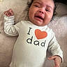 baby, crying, infant, onesie, clothing, text, heart_symbol, blanket, soft_texture, person, child, indoor, expression, emotion, toddler, skin, hand, face, head, cute