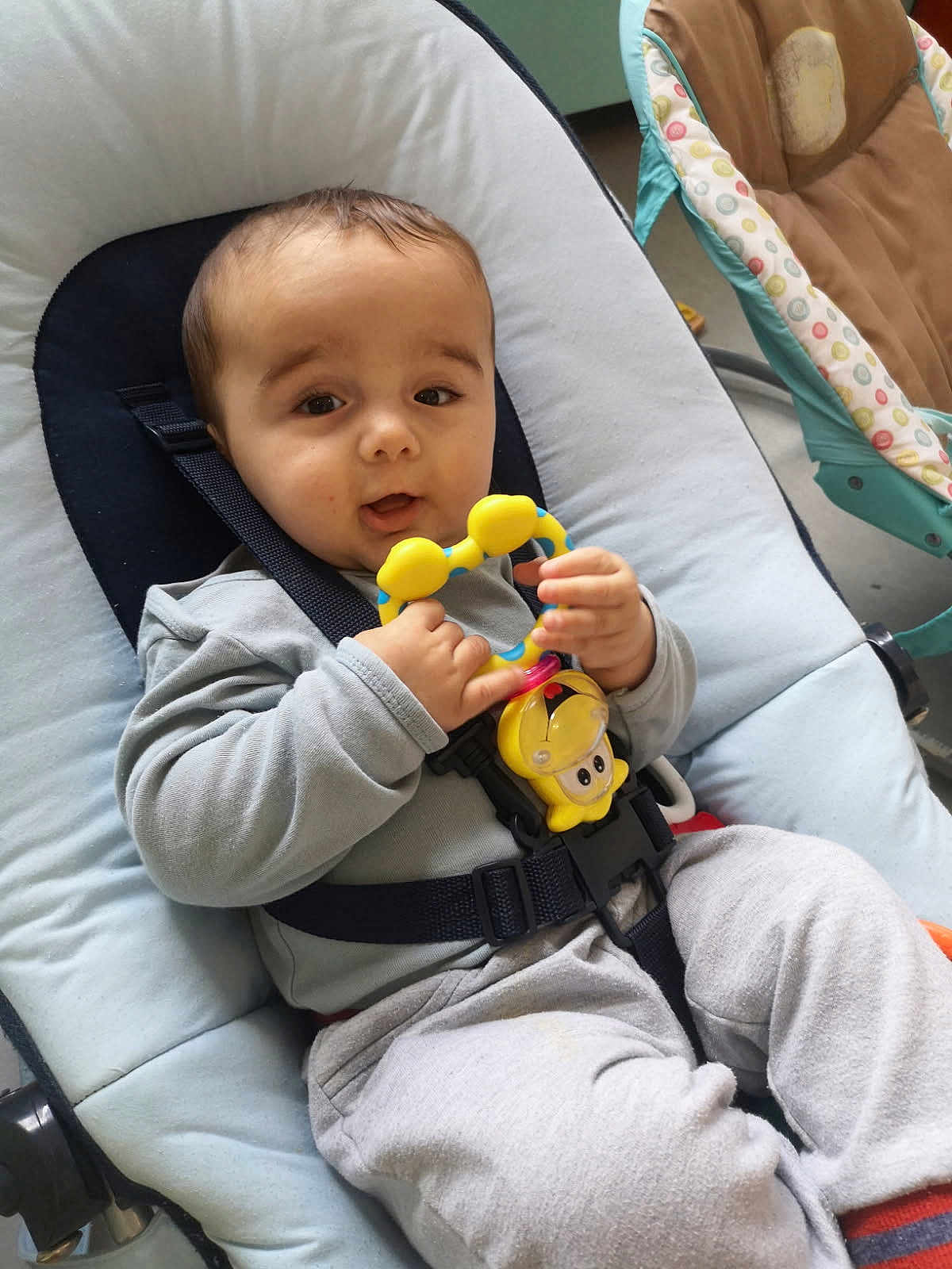 Vincenzo participe au concours pour gagner de l'argent avec cette photo : baby, infant, toy, baby_rocker, seat, clothing, straps, cushion, indoor, child, person, cute, happy, playful, grey_pants, long_sleeve_shirt, floor, baby_accessory, relaxing, young_child