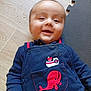 baby, child, smiling, navy_blue_clothing, whale_patch, boat_patch, floor, wooden_floor, foam_mat, portrait, infant, happy, cute, lying_down, face, head, hand, buttoned_clothing, indoors, casual