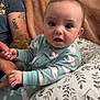 baby, child, pajamas, hand, tattoo, pillow, blanket, indoor, person, face, expression, holding, comfort, pattern, clothing, adult, skin, seated, closeup, home