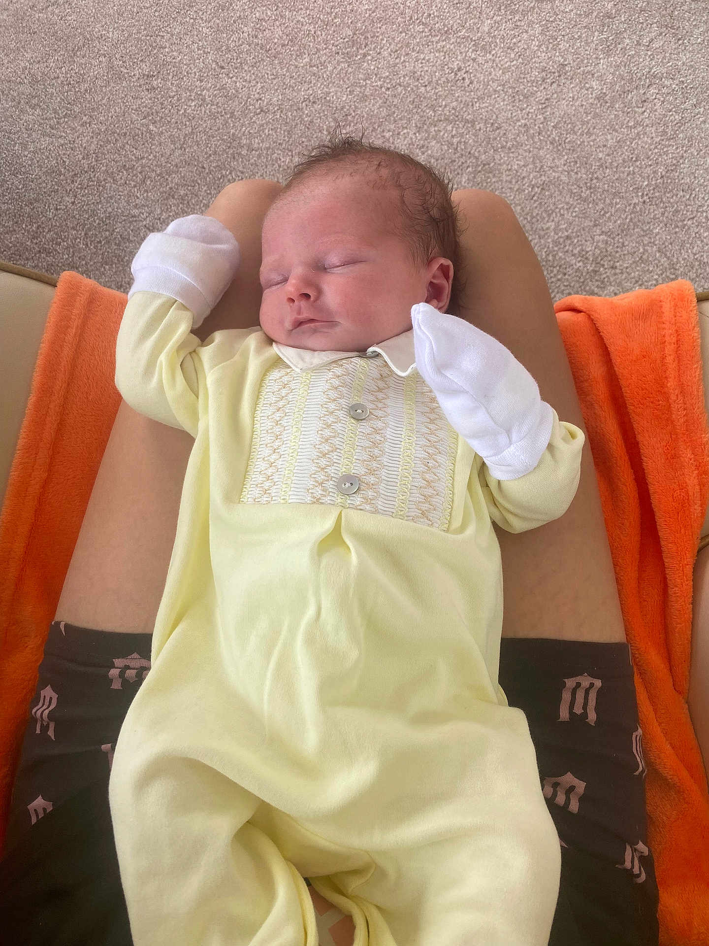 Terry joined the competition — help win amazing prizes! baby, newborn, sleeping, infant, yellow_onesie, mittens, person, lap, orange_blanket, carpet, indoor, resting, cute, peaceful, soft_fabric, child, human, portrait, relaxing, comfort