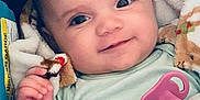 Olivia joined the competition — help win amazing prizes! baby, infant, smile, blanket, pacifier, clothing, hand, face, eyes, cute, child, indoors, portrait, baby_carrier, soft_texture, cozy, young, person, happy, closeup