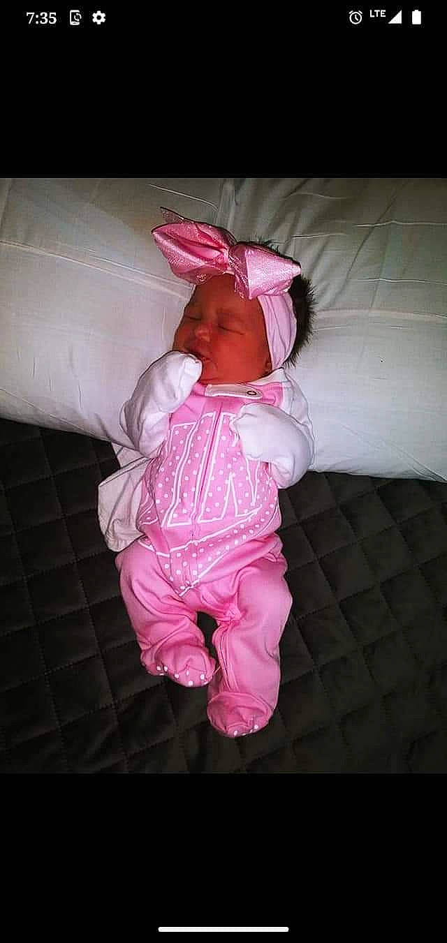 Ava is registered to the contest to win money with this photo: baby, baby_products, baby_toddler_clothing, cheek, child, comfort, darkness, eye, face, flooring, head, headwear, linens, magenta, pattern, person, pink, purple, room, sleeve