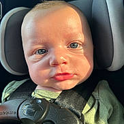 Bentley is registered to the contest to win money with this photo: baby, child, car_seat, harness, blue_eyes, green_shirt, infant, close_up, face, seatbelt, safety, portrait, skin, headrest, sunlight, expression, person, young_child, seat, indoor